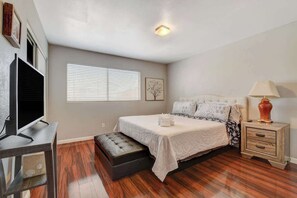 A bedroom with a bed, a TV, a nightstand, and a window with blinds.