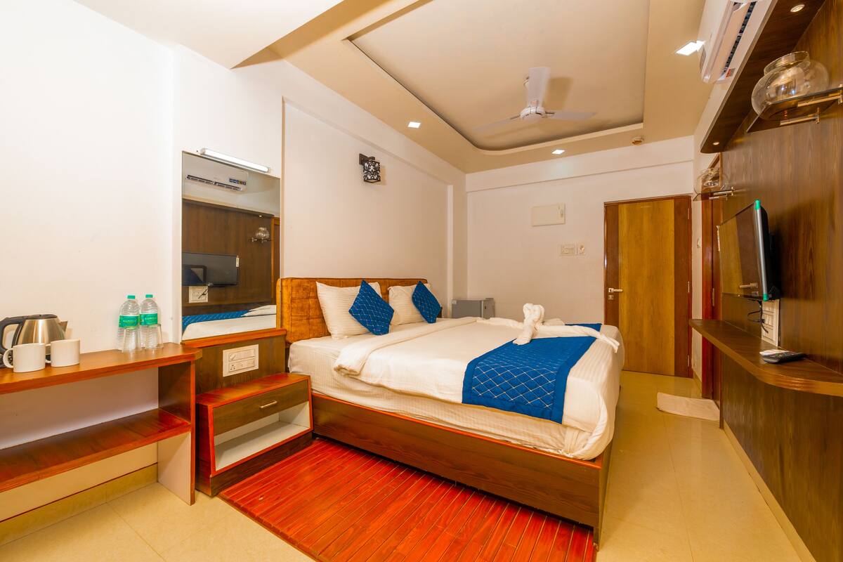 A hotel room with a wooden bed, a desk with a mirror, a TV, and a small kitchenette.
