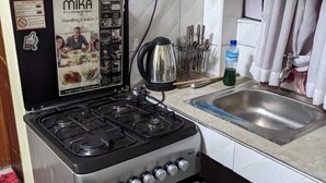 A kitchen with a standing cooker, a kettle, and a sink. - Eilarose Suites (Ruiru)