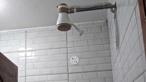 Een douche met een handdouche aan de muur bevestigd, een zichtbare afvoer en een betegelde muur met een baksteenmotief.