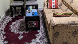 A room with two wooden chairs, a small table with a box and remote, a patterned sofa, and a red and white rug. - Eilarose Suites (Ruiru)