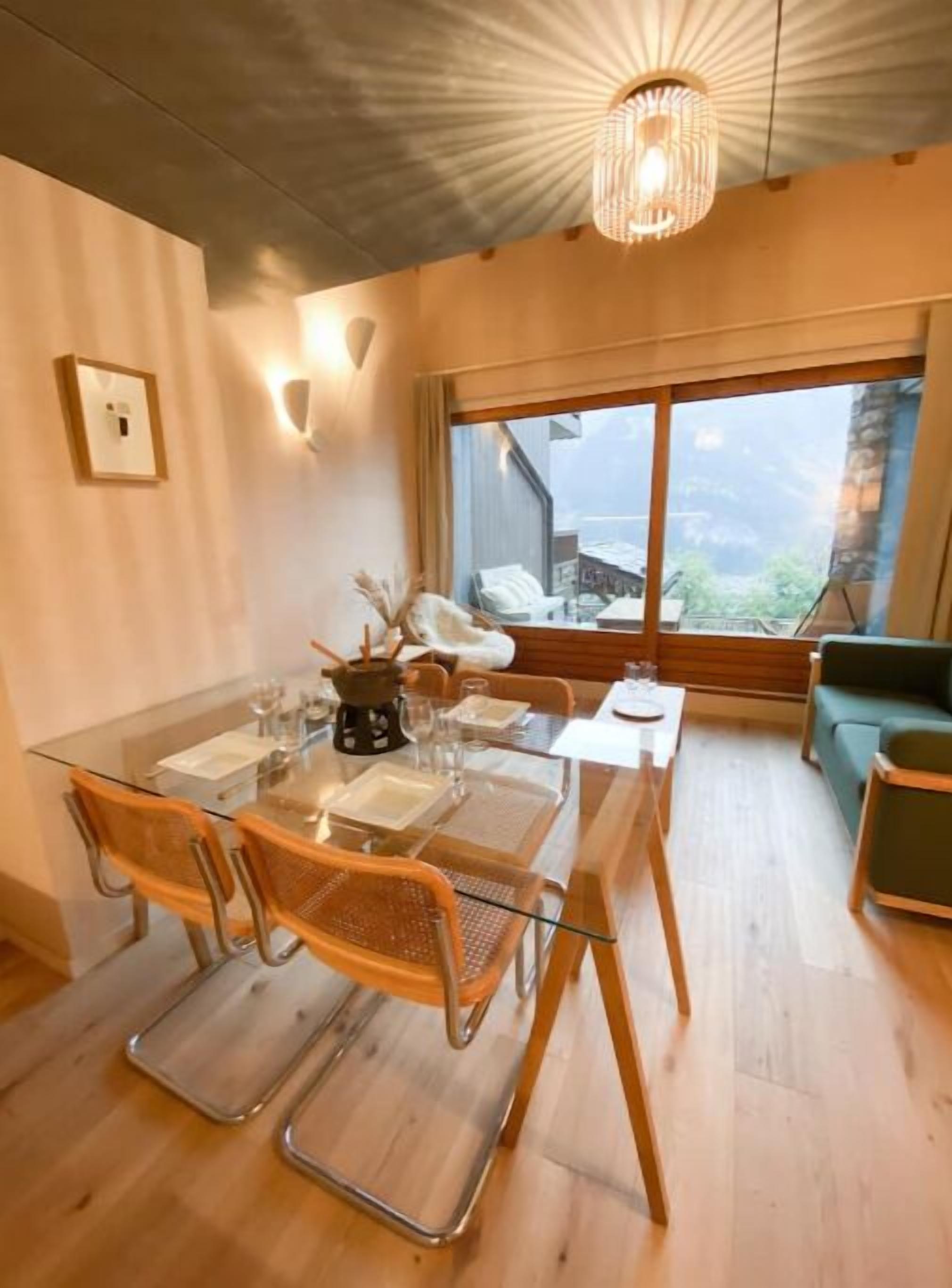 Un comedor con mesa de vidrio, sillas de madera y una lámpara moderna.