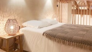 Une chambre confortable avec un plafond en bois, un lit recouvert de draps blancs, un plaid à motifs et un luminaire fixé au mur.