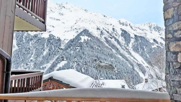 Un balcon en bois avec un mur en pierre, donnant sur une montagne enneigée.