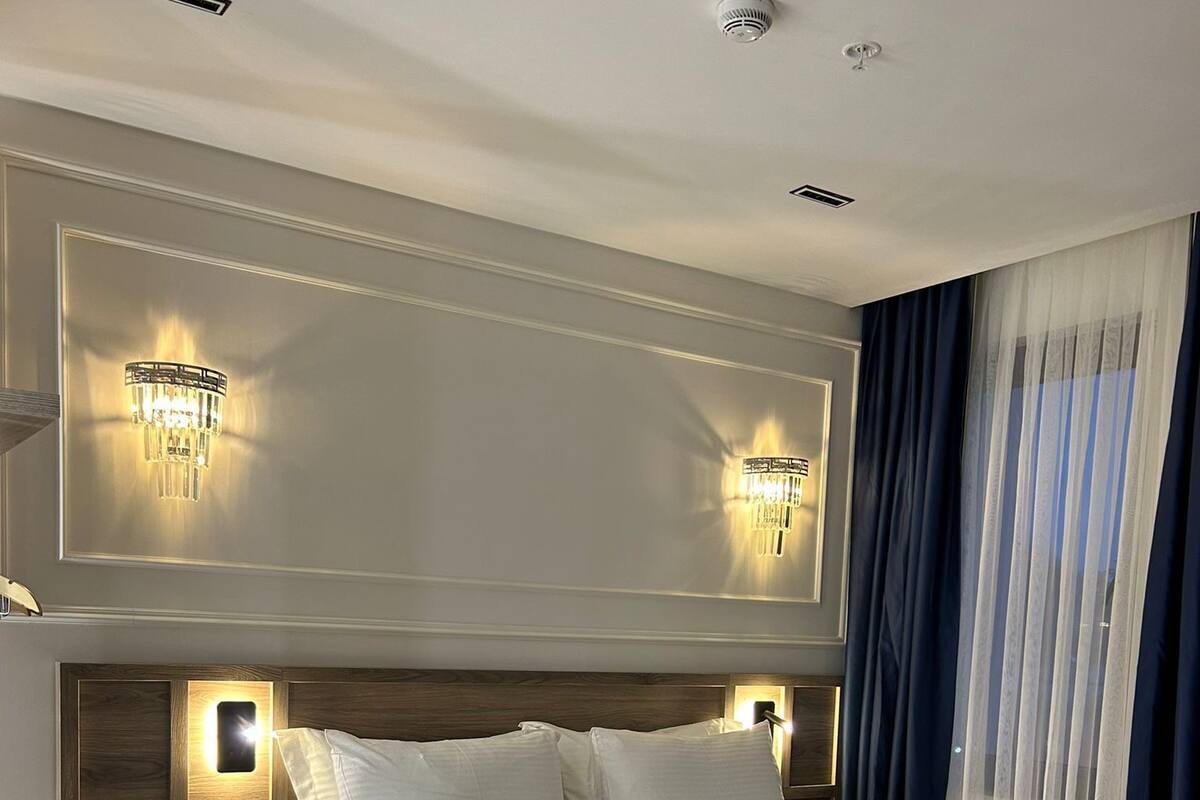 A hotel room with a large bed, bedside tables, a desk, and two wall-mounted lights.