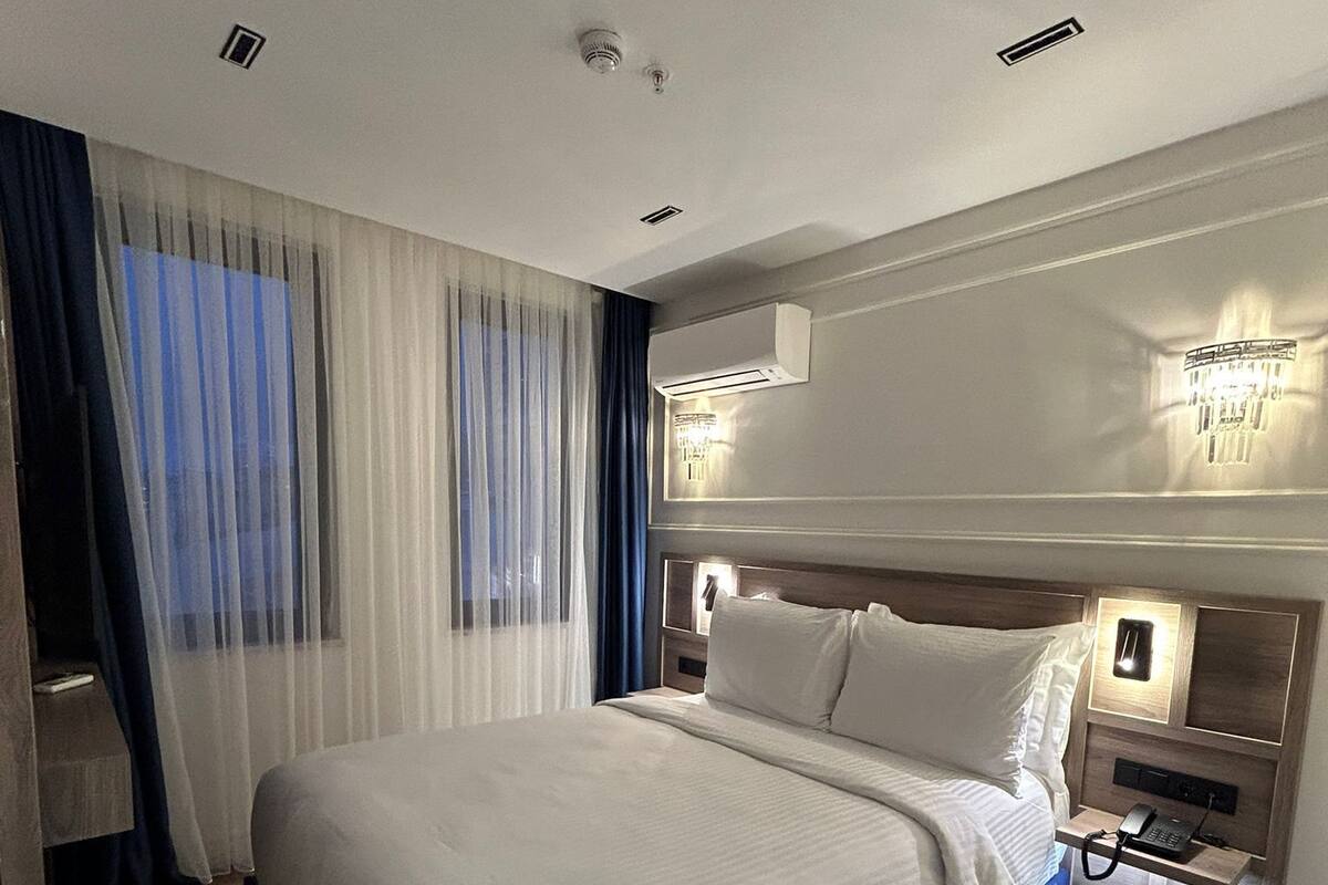 A modern hotel room with a large bed, a bedside table with a lamp, and an air conditioning unit on the wall.