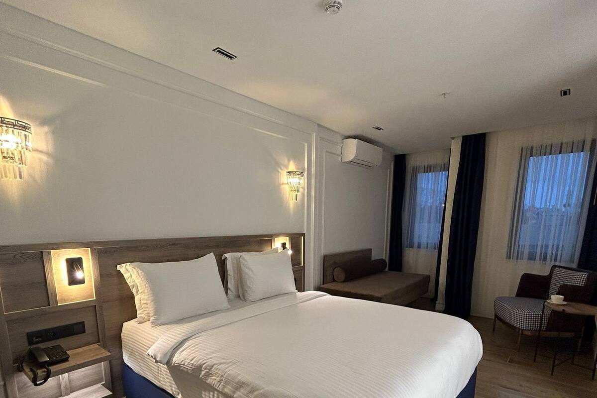 A modern hotel room with a large bed, bedside tables, a desk, and a chair.