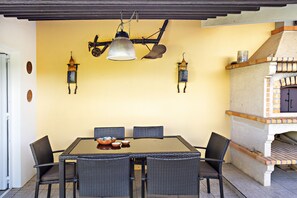Un comedor con una mesa, sillas, una lámpara colgante y un horno de ladrillo.
