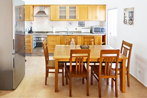 A kitchen with wooden cabinets, a stainless steel refrigerator, a microwave, and a dining table with chairs.