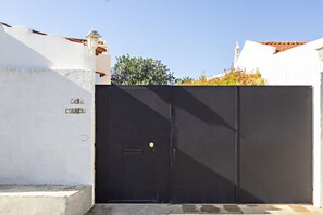 A black metal gate with a small yellow button, a white wall with the text "CASA CORREIA" above it, and a clear blue sky in the background.