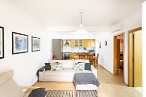 Een woonkamer met een bank, een salontafel en een vloerkleed. Achtergrond is een keuken met houten kastjes en een magnetron.