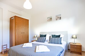 Una habitación de hotel con una cama grande, un armario de madera, dos mesitas de noche con lámparas y una obra de arte en la pared.