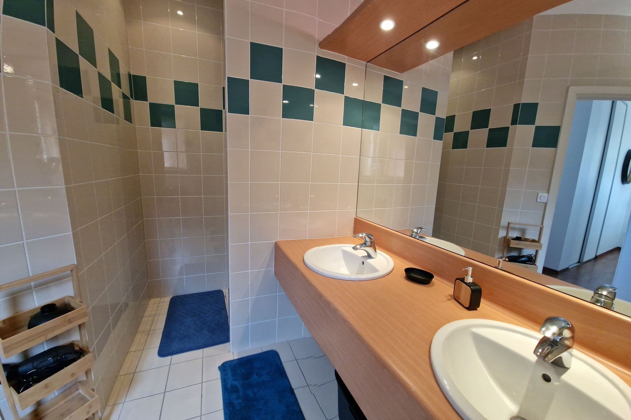 A bathroom with a wooden vanity, two sinks, a mirror, and a shower area.