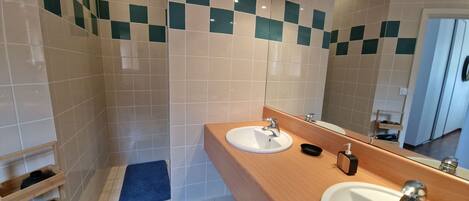 A bathroom with a wooden vanity, two sinks, a mirror, and a shower area.