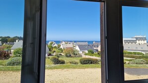 A view through a window of a coastal residential area with houses, greenery, and a clear blue sky. - Flat in Primel with Sea View & Beaches Nearby (Plougasnou)