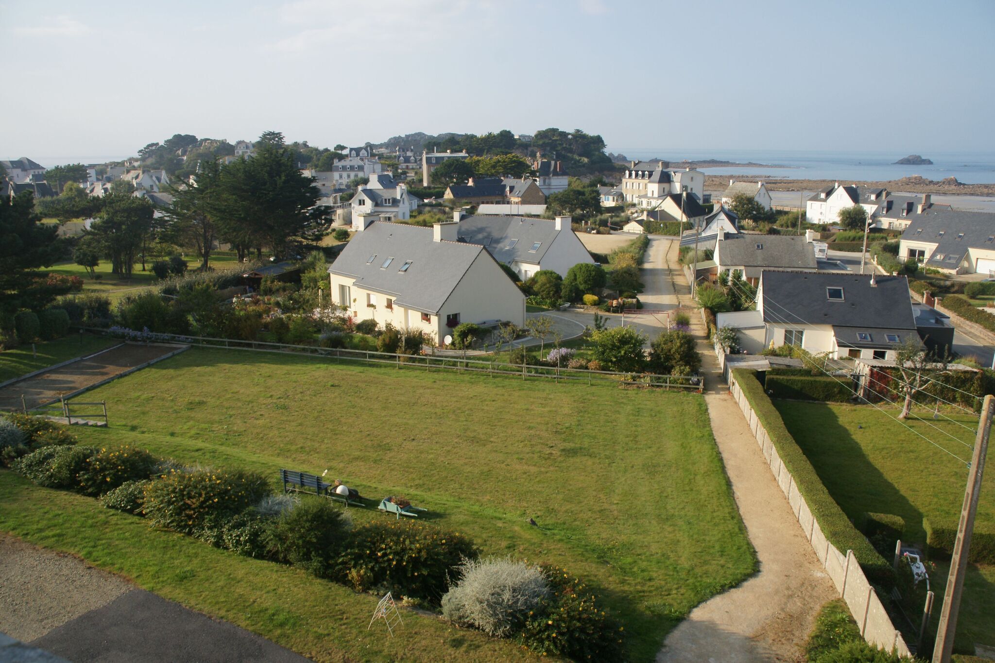 Zona residencial com casas, um campo gramado e vista para o mar.