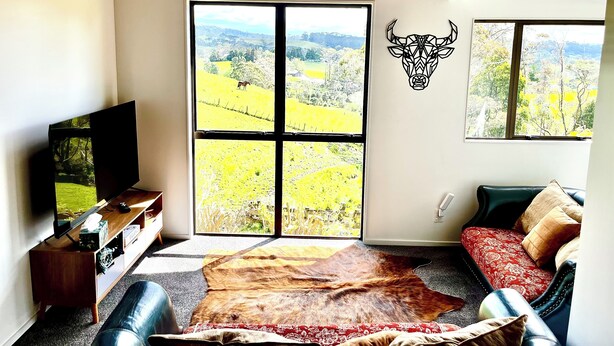 Un salon doté d’une grande fenêtre, d’une décoration murale représentant une tête de taureau, d’un canapé en cuir et d’un téléviseur posé sur un meuble en bois.