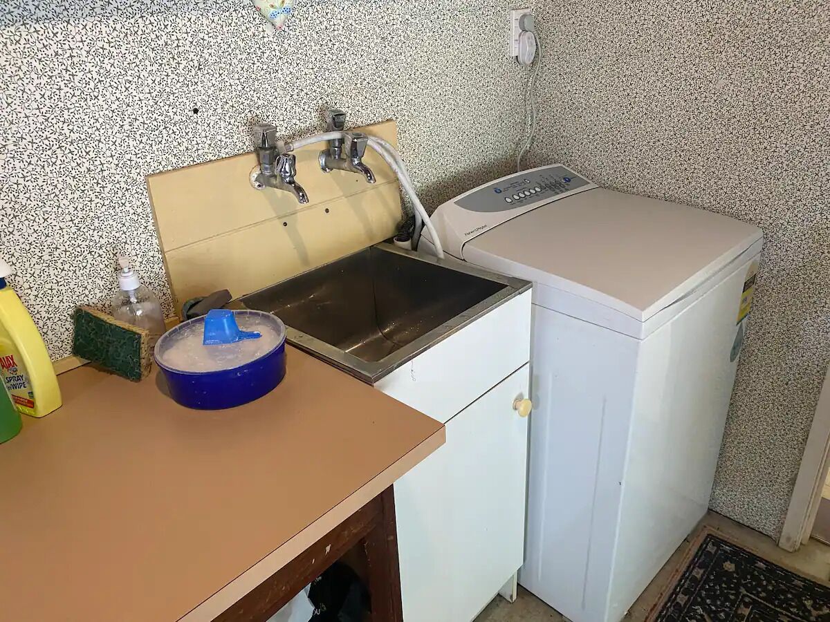 A compact kitchen with a sink, a washing machine, and cleaning supplies.