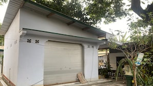 Un bâtiment blanc avec une fenêtre fermée, entouré de verdure et de matériaux de construction.
