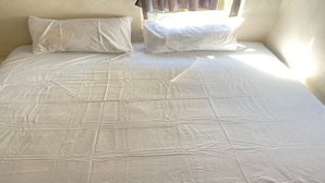 Un lit avec un drap blanc et deux oreillers, une fenêtre avec des rideaux et un mur uni.