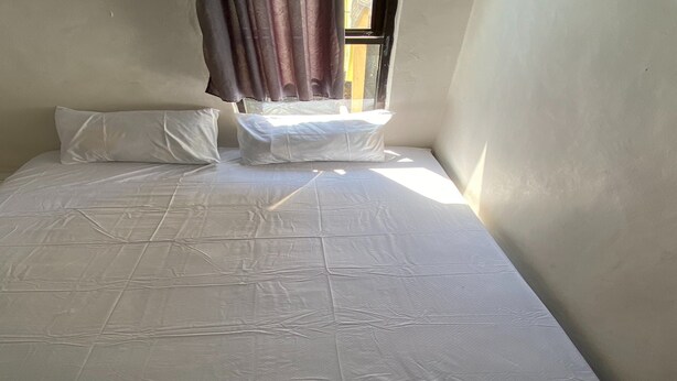 Un lit simple avec un matelas blanc et deux oreillers, une fenêtre avec des rideaux et un mur uni.