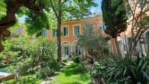 Un jardín exuberante con un sendero que conduce a un edificio de ventanas arqueadas y tejado de tejas.