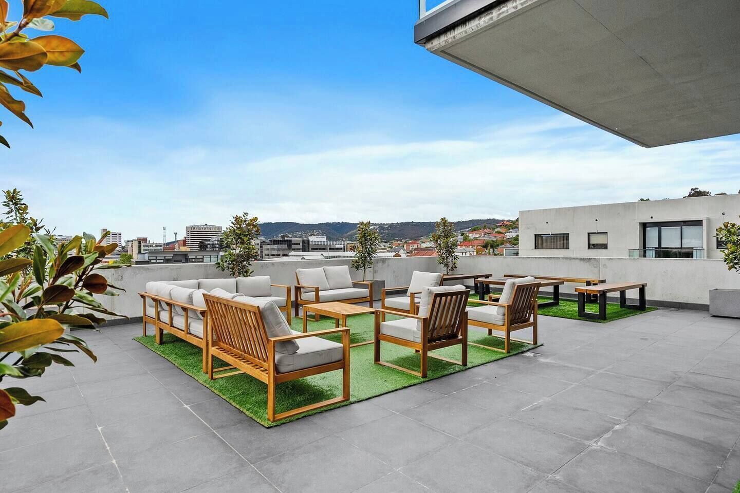 Une terrasse sur le toit avec des sièges extérieurs, une vue sur la ville et un bâtiment moderne en arrière-plan.