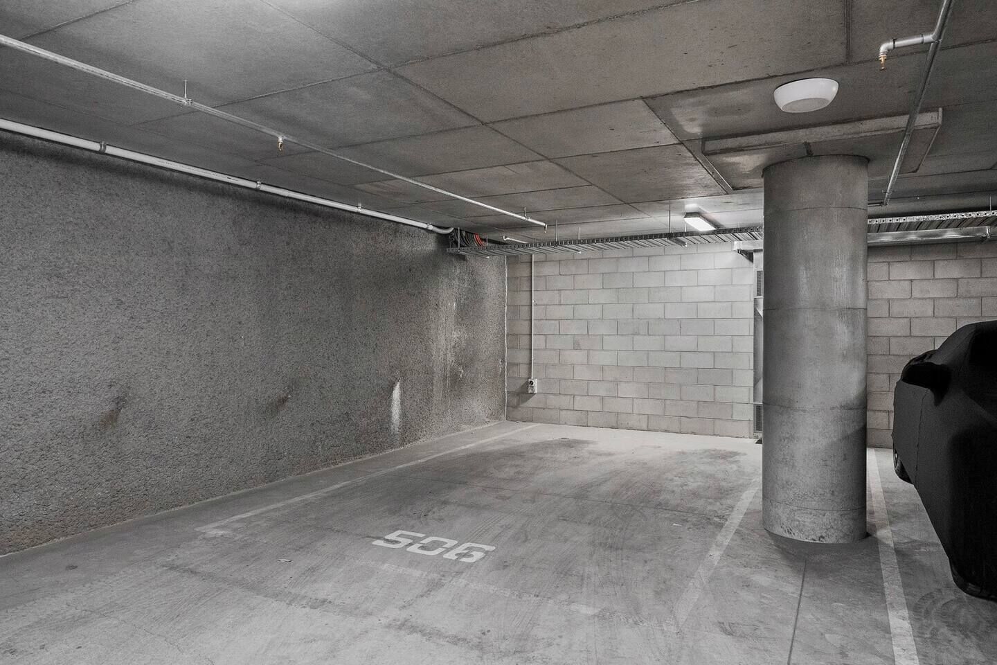A parking garage with concrete walls, a pillar, and a car covered with a tarp.