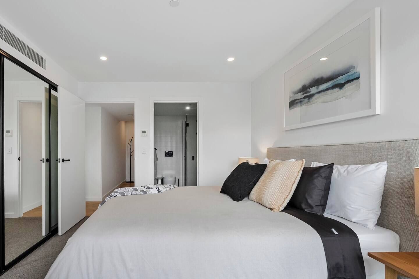 A modern bedroom with a large bed, a headboard, and a painting on the wall.