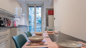 A modern kitchen with white cabinets, a dining table set with bowls and wine glasses, and a window overlooking a cityscape. - Amendola House by Wonderful Italy (Turin)
