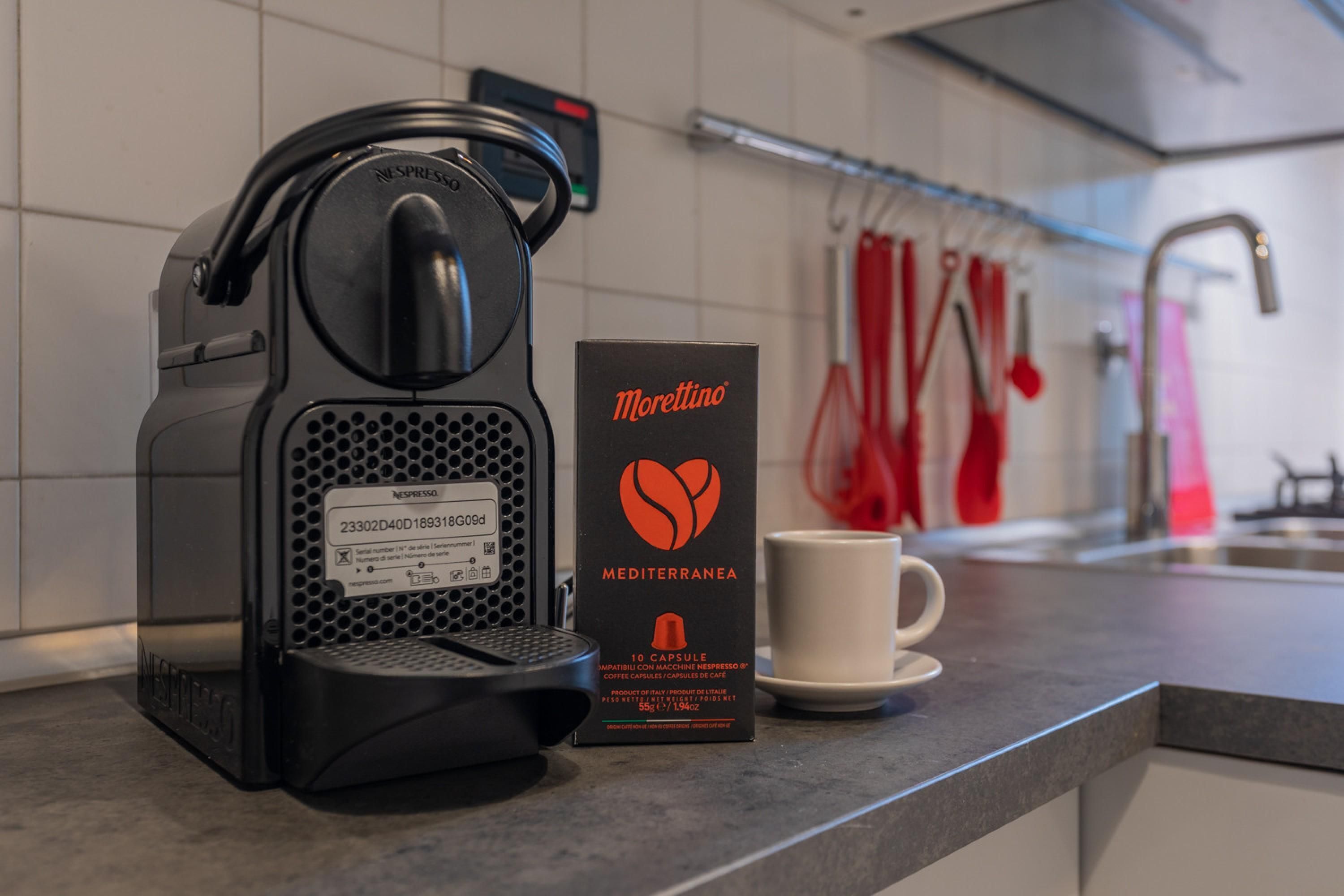 A Nespresso machine, a Morettino espresso capsule box, and a white cup on a kitchen counter.