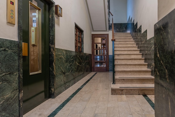 A marble-floored hallway with a staircase, an elevator, and a wooden door.