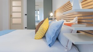 A neatly made bed with pillows, a bedside table with a lamp, and a door with frosted glass panels. - Amendola House by Wonderful Italy (Turin)