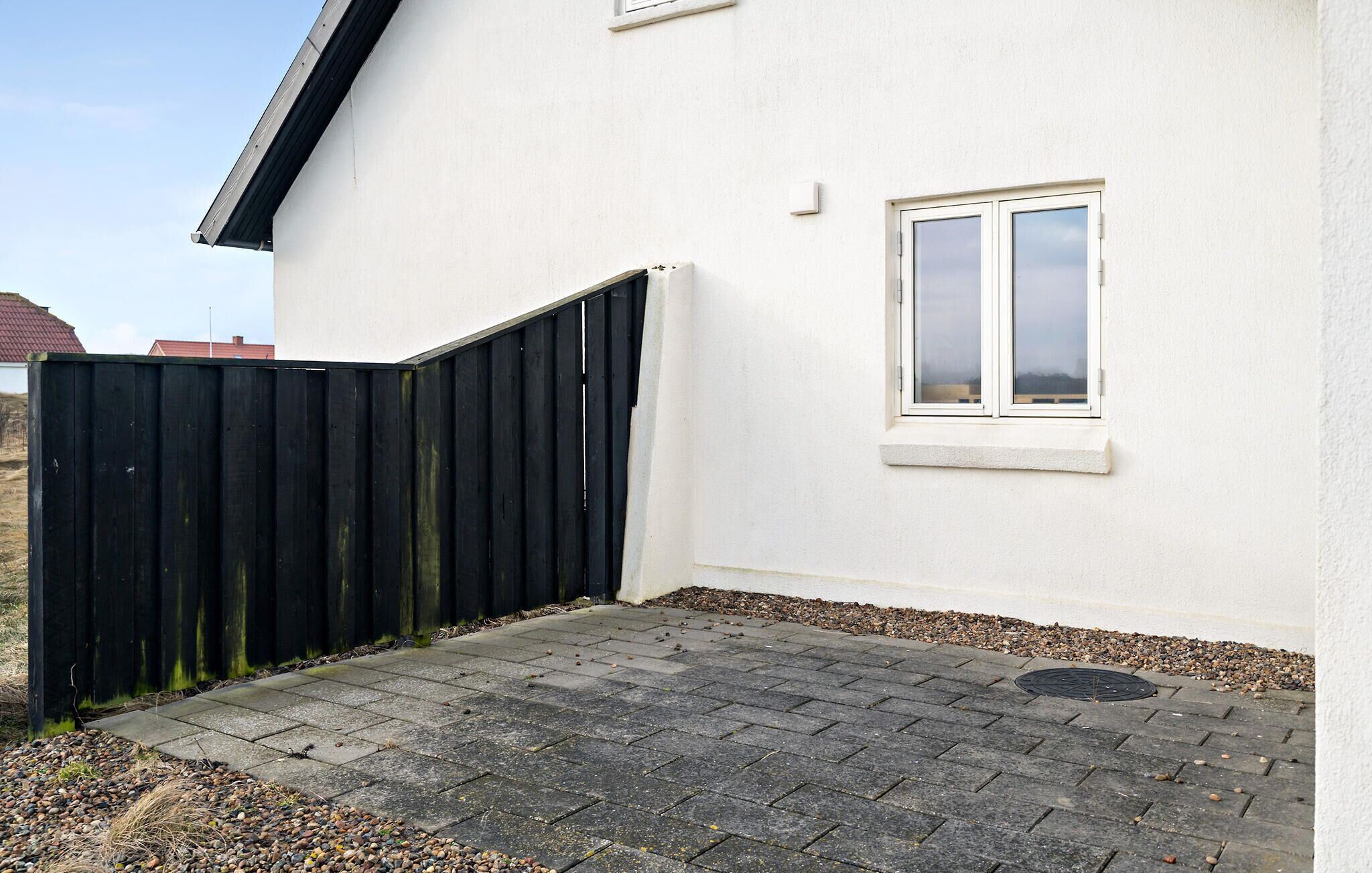 Un bâtiment blanc avec un portail en métal noir, une fenêtre et une zone pavée avec des petits cailloux.