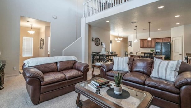 A spacious living room with two brown leather sofas, a coffee table, and a staircase leading to an upper level. - Zions & St.George Adventure Base (Washington)