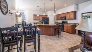 A spacious kitchen with wooden cabinets, a central island, pendant lighting, and a dining area with dark wooden chairs. - Zions & St.George Adventure Base (Washington)