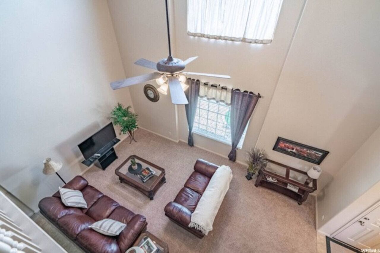 A living room with a ceiling fan, a television, a sofa set, a coffee table, and a window with curtains.