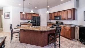 A kitchen with granite countertops, wooden cabinets, a central island, and pendant lighting. - Zions & St.George Adventure Base (Washington)