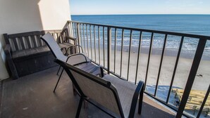 A balcony with a view of the ocean, a wooden bench, and a chair. - Oceanview Oasis 7th Floor King Room (Pawleys Island)
