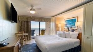 A hotel room with a large bed, a desk with a telephone, a chair, a balcony with a view, and a painting on the wall. - Enchanting Atlanic View Oceanfront King Room 7th Fl (Pawleys Island)