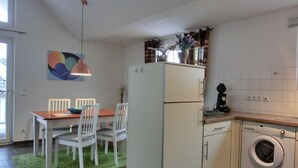 A compact kitchen with a refrigerator, a washing machine, and a dining area with chairs and a table. - Strandnahe Lage - MIT Balkon - Kaminofen- Wlan (Graal-Müritz)