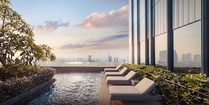 Área de piscina no terraço com espreguiçadeiras e vista para o horizonte da cidade.