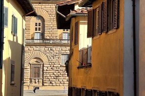 A narrow street with historic buildings, a stone archway, and a person walking.