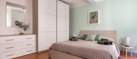 Un dormitorio con cama, cómoda, espejo, planta y un cuadro en la pared.