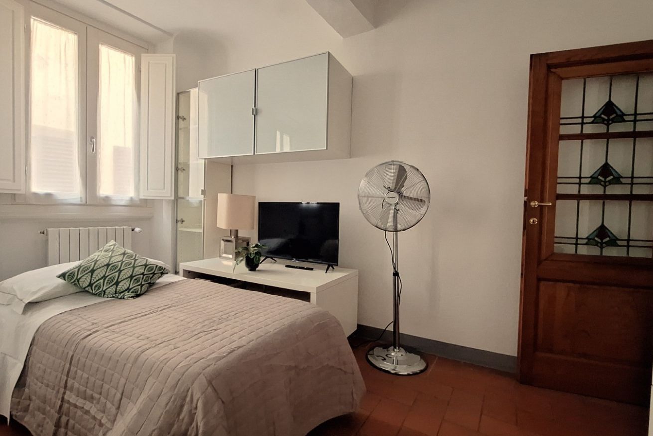A bedroom with a bed, a TV, a fan, and a cabinet.