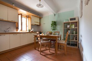 A kitchen with wooden cabinets, a dining table with chairs, a hanging plant, and a microwave shelf.
