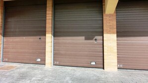Three closed garage doors with metal handles and a brick wall.