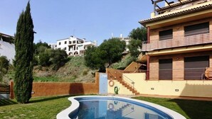 A swimming pool surrounded by a well-maintained lawn, with a staircase leading to a building with a tiled roof.