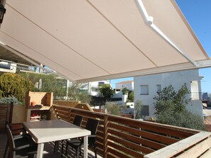 Um pátio externo com mesa e cadeiras, um banco de madeira e um toldo branco.