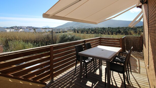 A wooden deck with a table and chairs, a large umbrella, and a view of a town and mountains in the background.